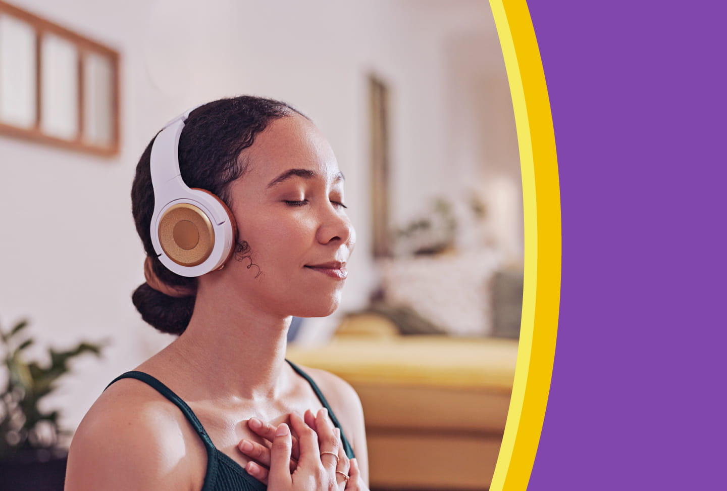 A young woman smiles with her eyes closed while she listens to headphones with her hands crossed over her heart
