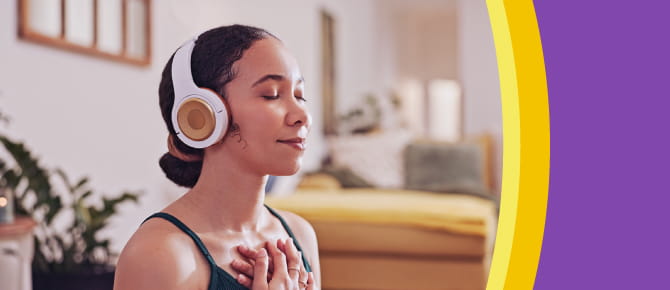 A young woman smiles with her eyes closed while she listens to headphones with her hands crossed over her heart