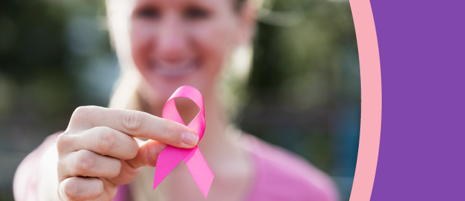 A woman holds a pink breast cancer awareness ribbon in her fingers