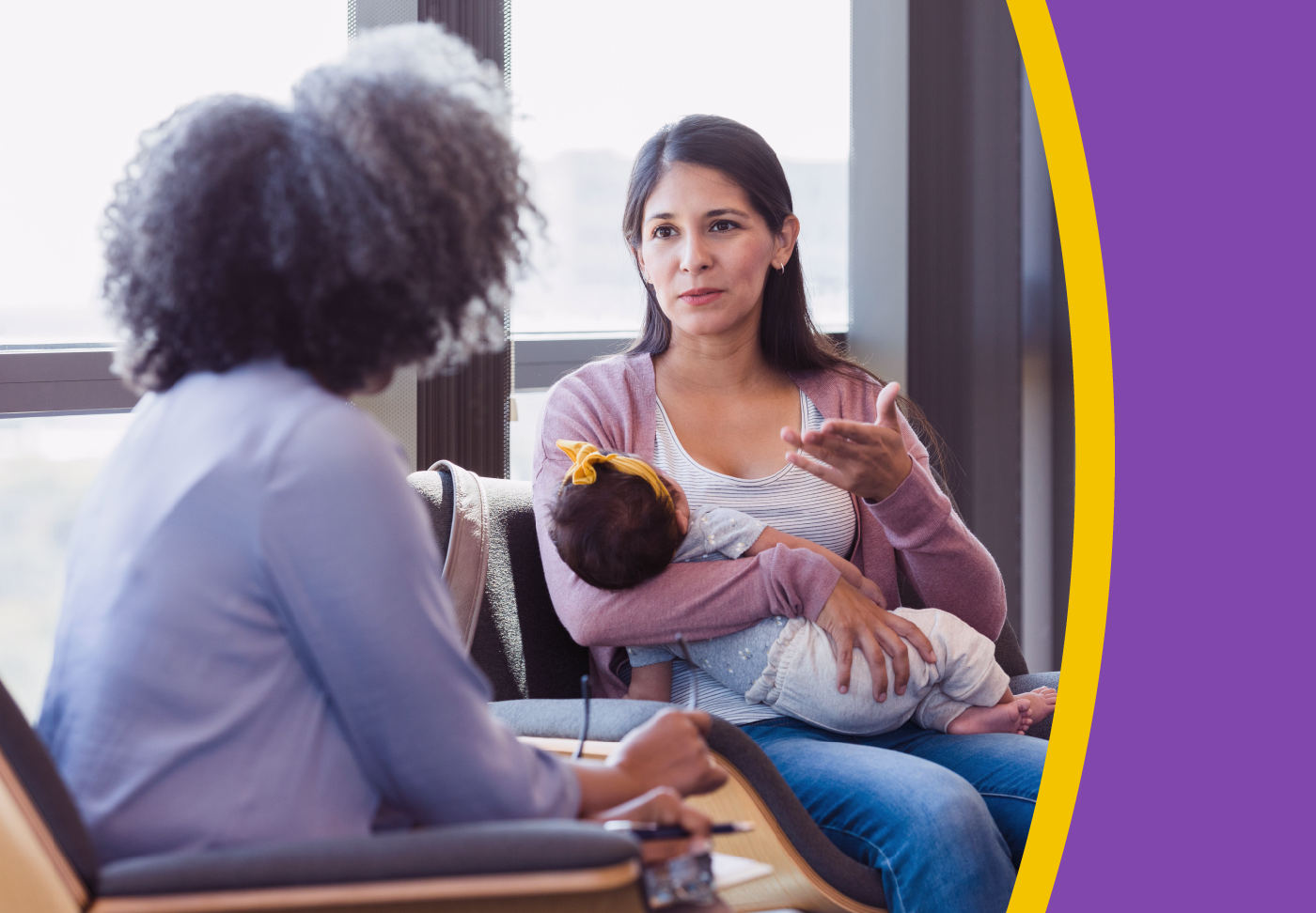 Person holding baby sitting and speaking with another person