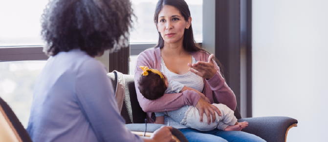 Person holding baby sitting and speaking with another person