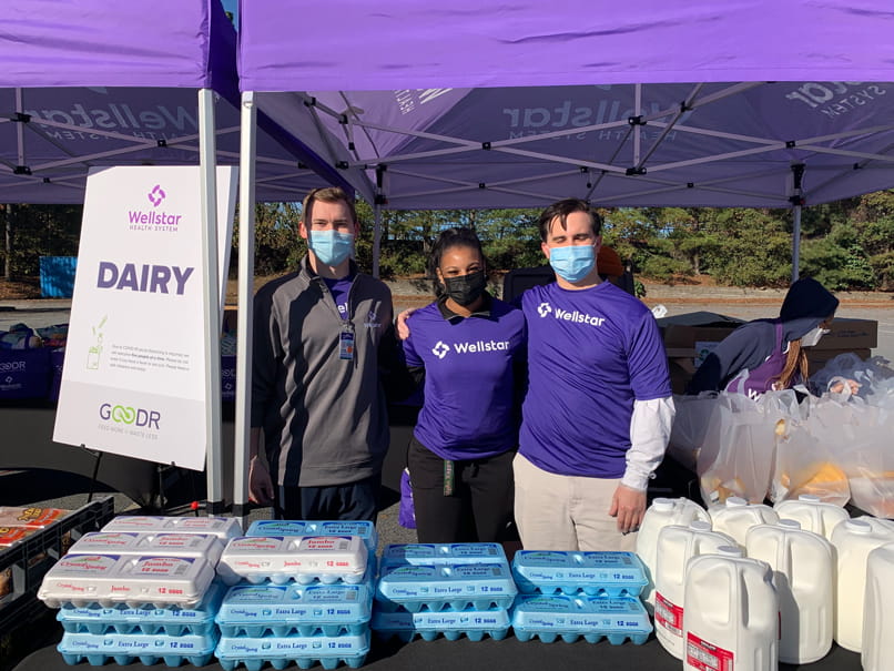 Three people wearing masks with cartons of eggs, sign reading "dairy"