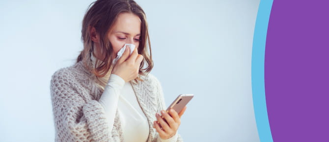Person blowing nose with tissue, looking at phone