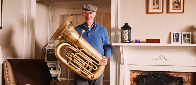 Frank Ryan with his tuba posed in front of his fireplace.