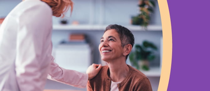Care provider shows compassion for a patient with a gentle shoulder touch and the patient returns a genuine smile.