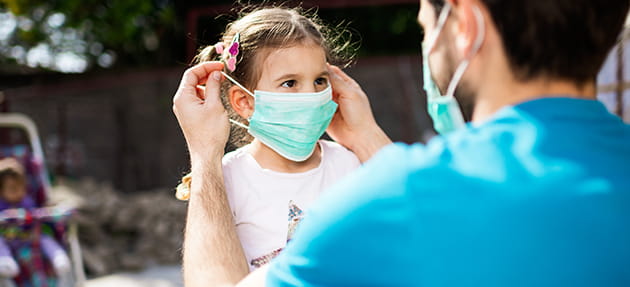 A father helping his daughter put on a face mask