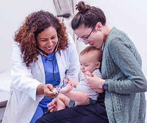 A smiling healthcare provider working with a mother and her baby
