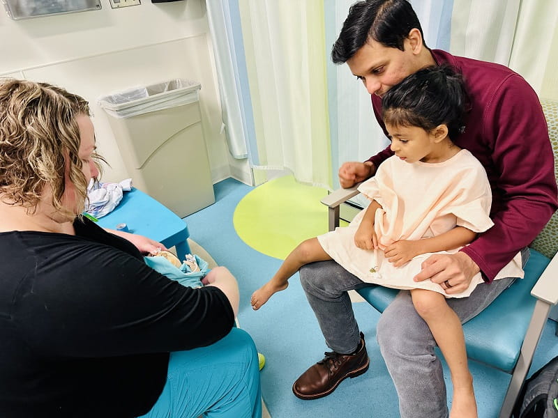Shows a Child Life Specialist sharing information about a medical procedure for a child to understand, using a doll to demonstrate.