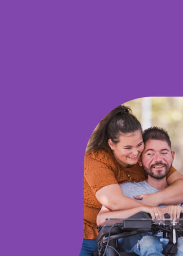 Woman hugging a man in a motorized wheelchair as both smile
